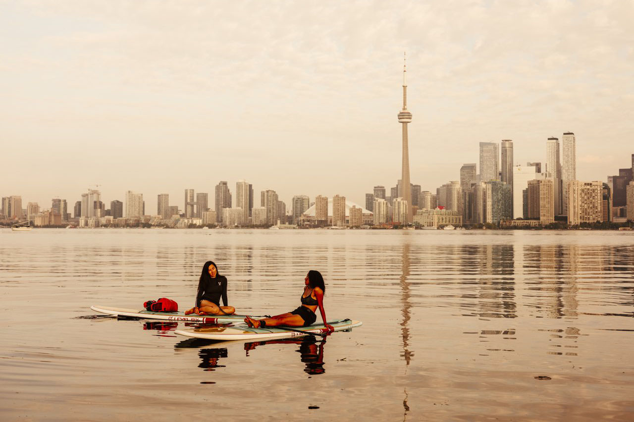 Two people on paddleboards with the tall buildings of the city of Toronto on the background