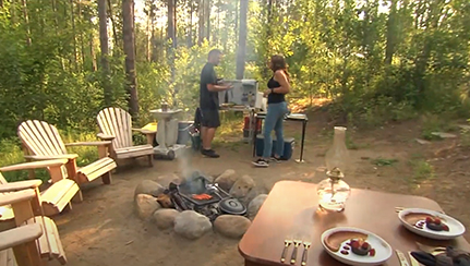 Deux personnes discutant autour d’un feu dans un emplacement de camping où la table est dressée.