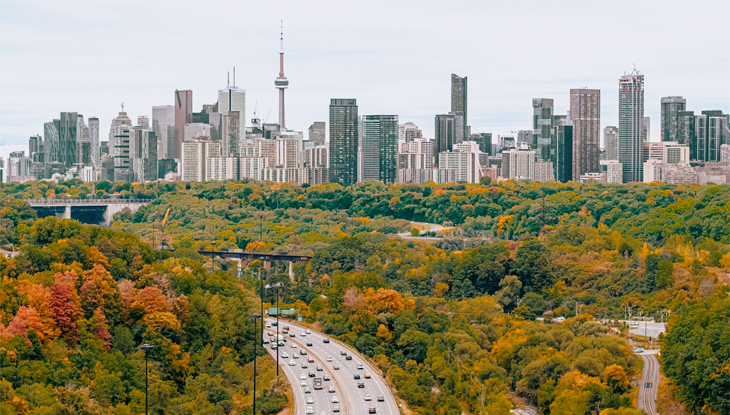 Vue du paysage urbain d'une autoroute menant vers l'horizon de Toronto entourée d'une forêt avec un feuillage d'automne.