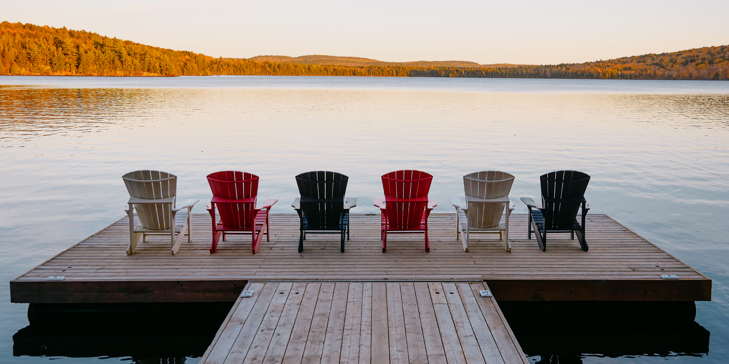 Six chaises Muskoka vides sur un long quai, sous un ciel coloré au crépuscule, au Killarney Lodge, dans le parc Algonquin.