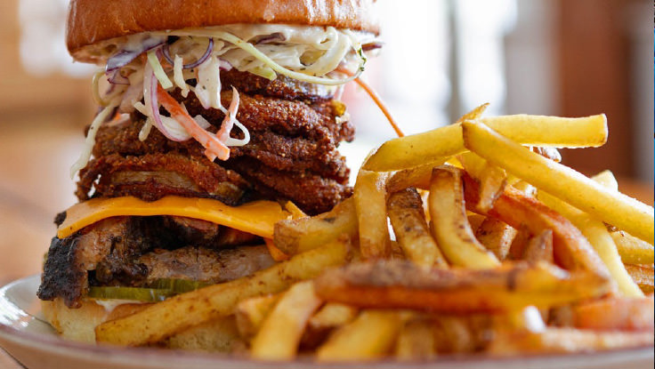 Una hamburguesa alta con papas fritas en un plato.