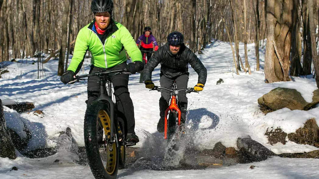 Drei Radfahrer fahren auf Fatbikes einen verschneiten Weg entlang.
