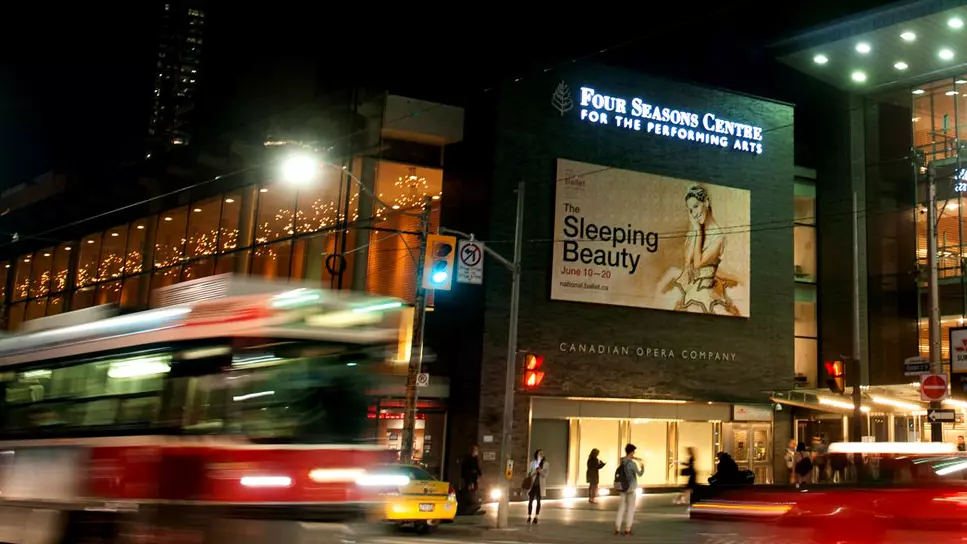 Un tranvía y el tráfico pasan frente a un gran cartel del ballet La Bella Durmiente en Toronto.