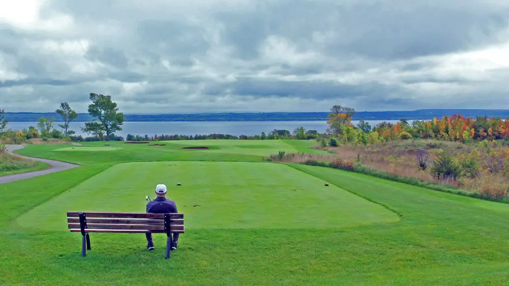 Ein Mann sitzt auf einer Bank mit Blick auf das Grün eines Golfplatzes.