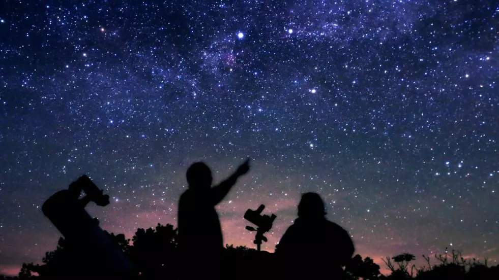 Silueta de dos personas señalando y mirando hacia las estrellas.