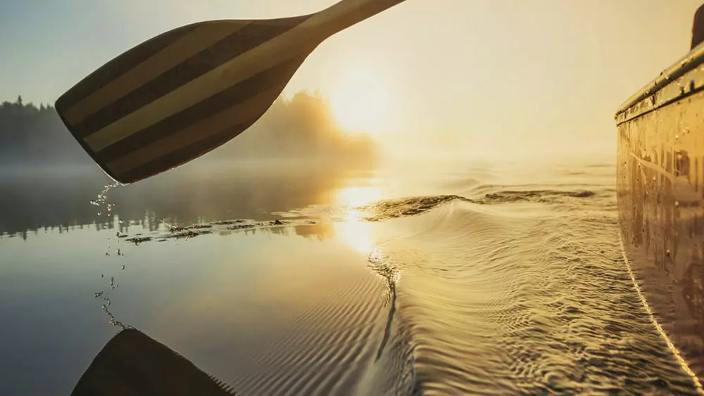 Un remo de canoa avanza suavemente por el agua hacia la puesta de sol.
