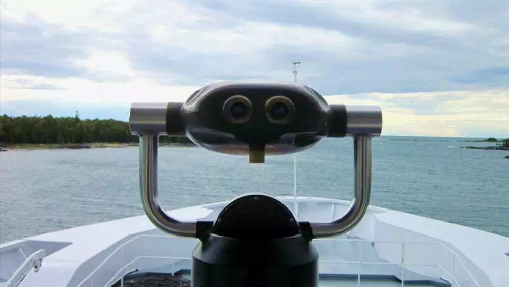 A viewfinder on the outside deck of a ferry overlooks the shoreline and lake ahead.