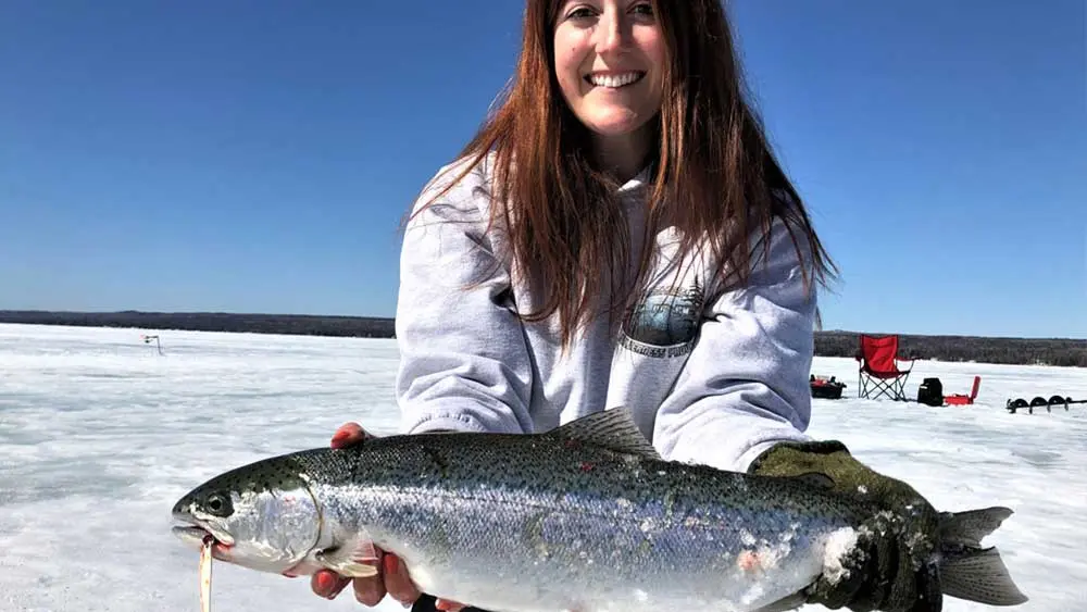 A woman holds up a large whitehead fish caught on a frozen lake