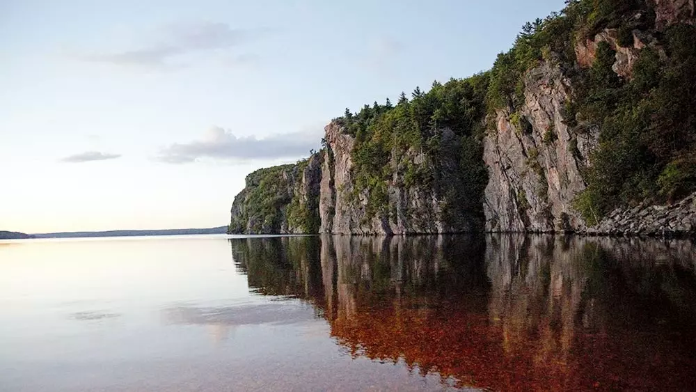 El reflejo de una enorme roca escarpada sobre las tranquilas aguas del Parque Provincial Bon Echo.