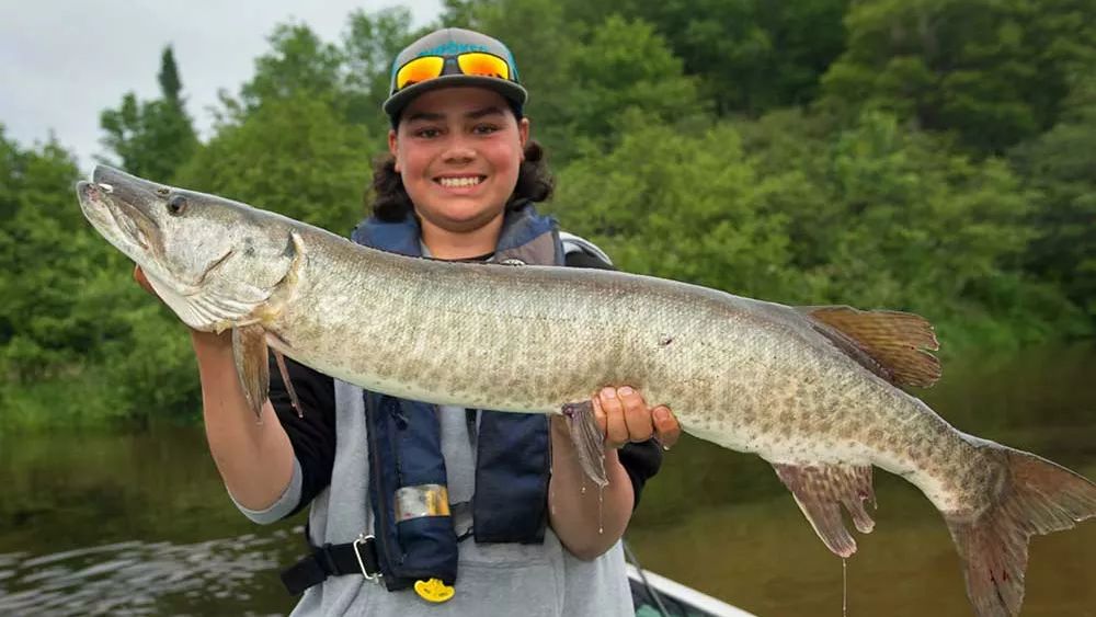 A young man in a boat holds a muskie caught in a back bay of Lake Huron's North channel
