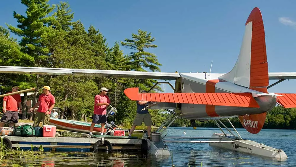 3人の男が水上飛行機に漁具を積み込んでいる。