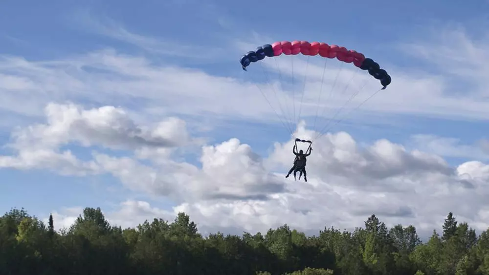 두 명의 스카이다이버가 들판에 낙하산을 내리고 착륙하는 모습.