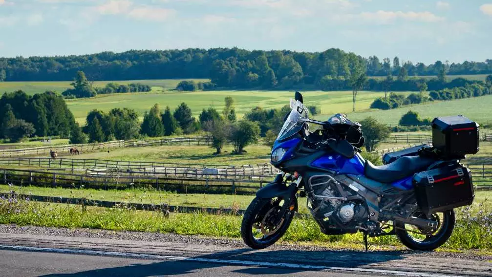 말 농장이 내려다보이는 시골 길가에 파란 오토바이가 주차되어 있습니다.
