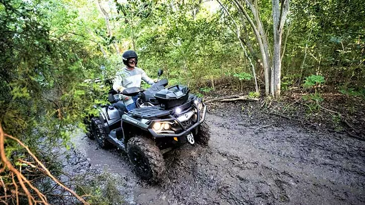 森の中の未舗装の道をATVに乗って走る人。