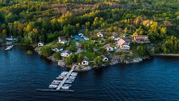 View of a fishing resort and cabins on the shore of a lake surrounded by forest.