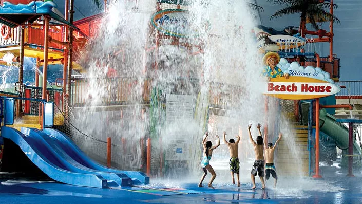 네 명의 어린이가 실내 워터파크의 물이 튀는 폭포 아래에서 놀고 있습니다.