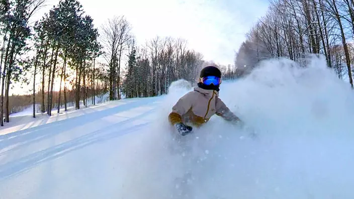 Eine Person fährt mit dem Snowboard einen von Bäumen gesäumten Hang hinunter.