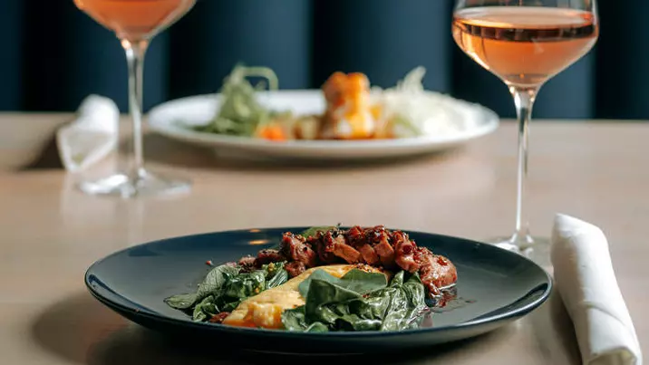 Auf einem Tisch stehen zwei Teller mit Essen und zwei Gläser Roséwein.