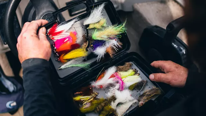 Vista de una persona abriendo una caja de moscas coloridas en su regazo en un barco.