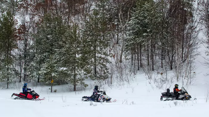 세 명의 라이더가 스노모빌을 타고 눈 덮인 산길을 따라갑니다.