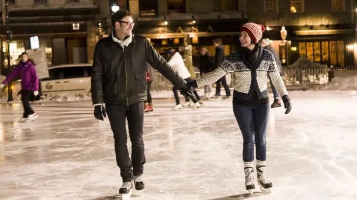 Two people holding hands and smiling at each other while ice skating at night.