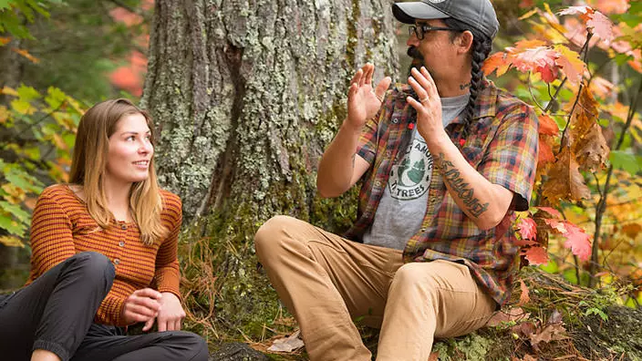 Un hombre y una mujer se sientan bajo un árbol en la temporada de otoño.
