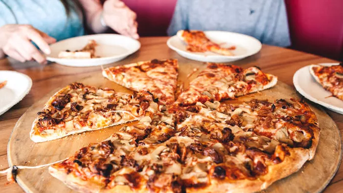 Se corta una pizza grande, de tamaño familiar, sobre una tabla de madera redonda para compartir.