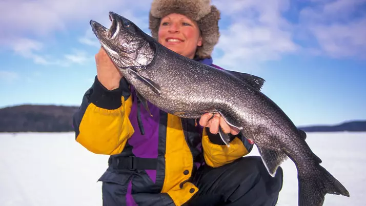 Une femme tient un gros poisson capturé lors d’un tournoi de pêche sur glace.