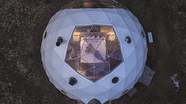 Aerial view of a person lying on a bed in a dome tent looking up through a skylight.