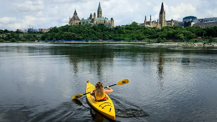 Una mujer en un kayak amarillo remando hacia la Colina del Parlamento en Ottawa.