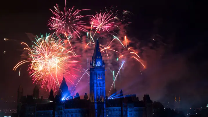 Une femme brandit un drapeau canadien sous un ciel illuminé par des feux d'artifice.
