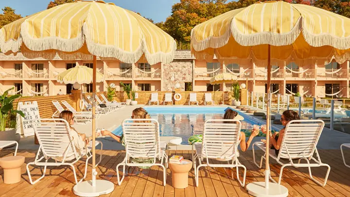 Quatre femmes relaxant sur des chaises longues au bord d’une piscine, sous des parasols jaunes.