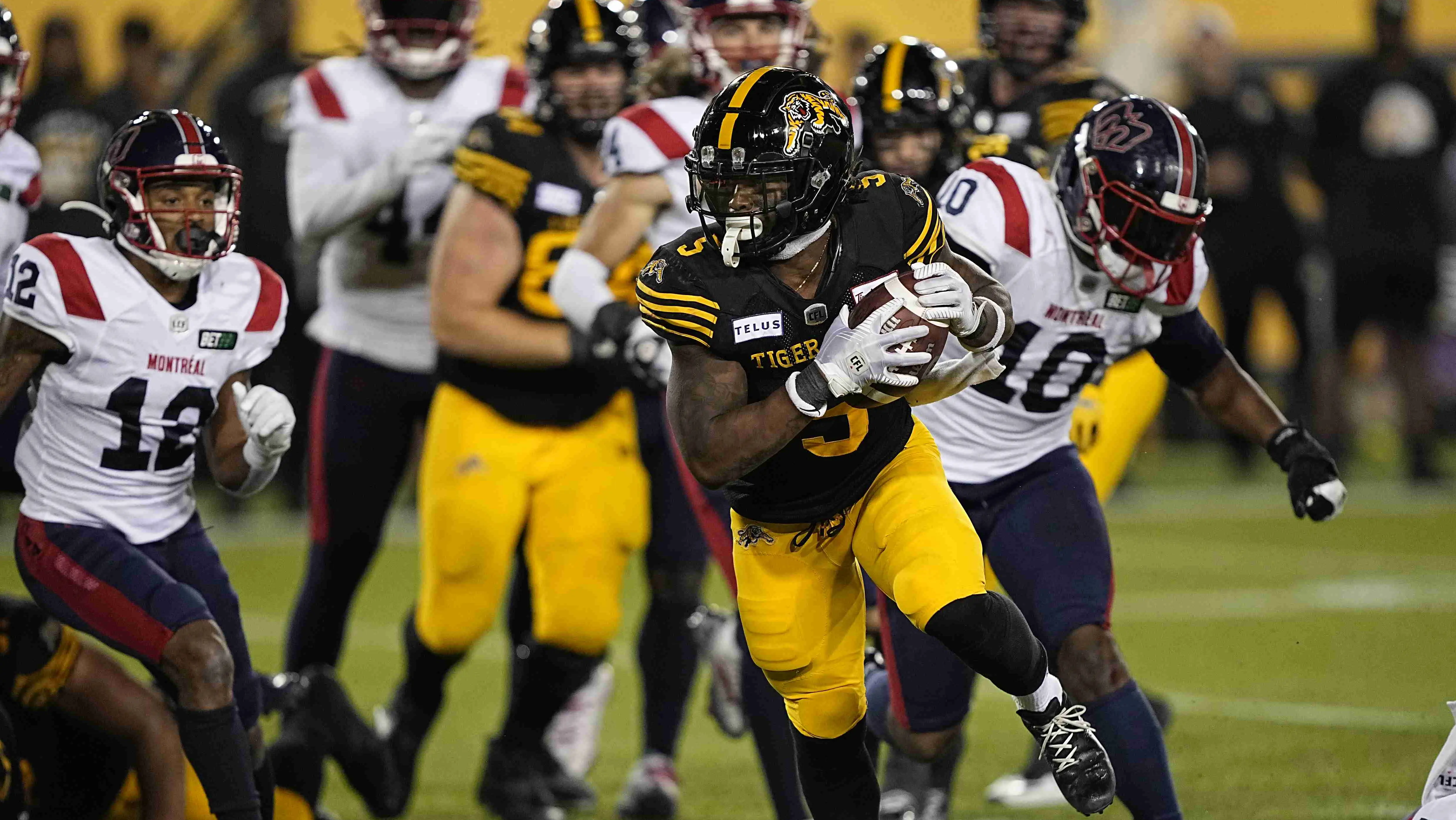 캐나다 프로 풋볼 선수가 타이거 캐츠 경기에서 공을 가지고 달리고 있다.