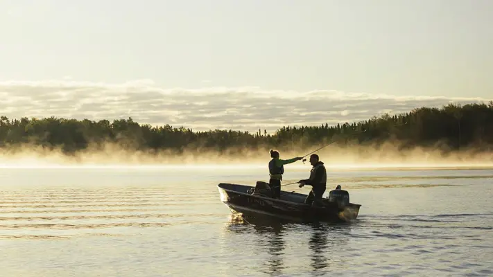 Zwei Angler angeln im Morgengrauen von einem Boot aus.