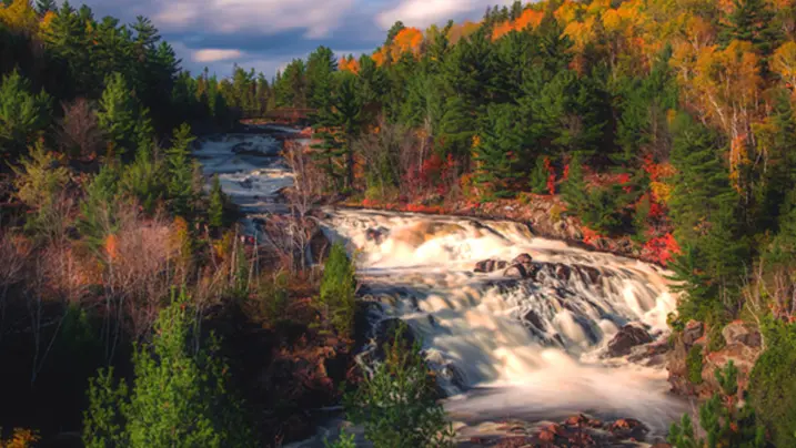 A waterfall cascades through forests ablaze with fall colour.