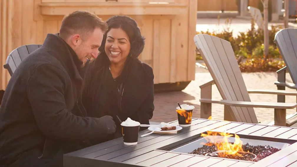 Una pareja se acurruca junto a una fogata al aire libre y disfruta de un chocolate caliente.