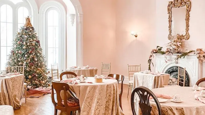 The dining room of a historical home is set with an elegantly decorated Christmas tree and several tables.
