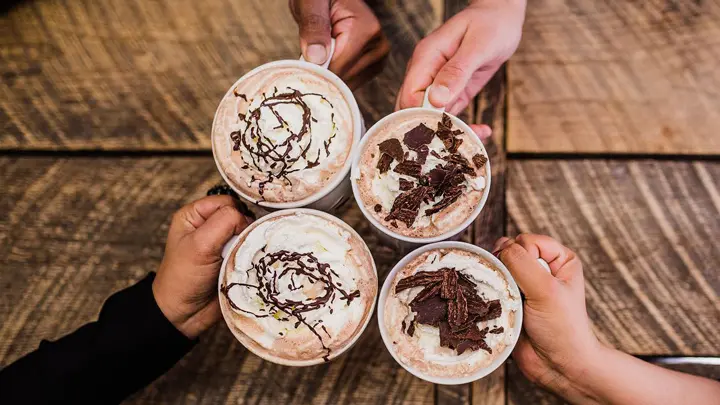 Four hands holding mugs of hot chocolate