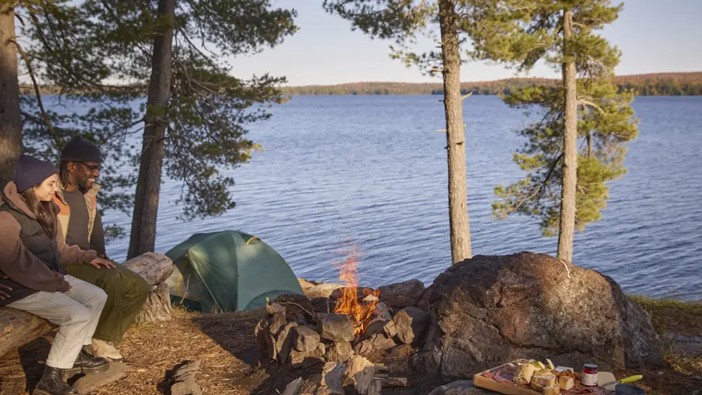 Zwei Personen sitzen zusammen vor einem Feuer auf einem Campingplatz im Algonquin Park.
