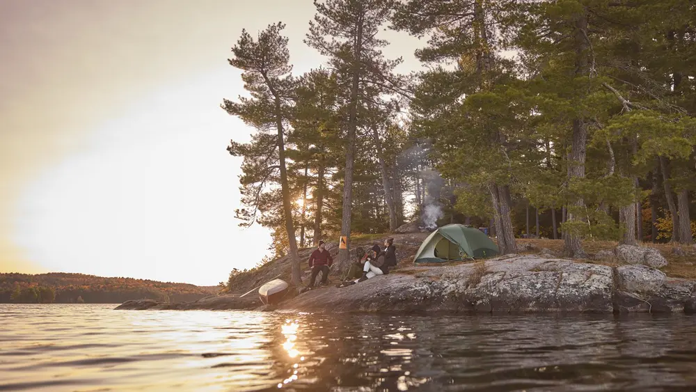 A group of campers sit on a rocky shoreline to watch the sunset in Algonquin Park.