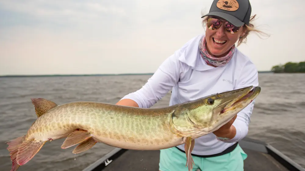 A woman holds up a large muskie on a fishing trip from Grassy Narrows Lodge.