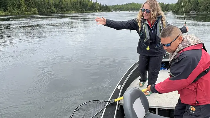ボートに乗っている男性が、釣り糸に触れている女性の前で漁網を持っている。