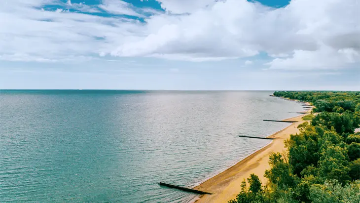 An aerial view of gorgeous blue-green water, a long sandy beach and lush green trees at Canatara Park Beach, Sarnia.
