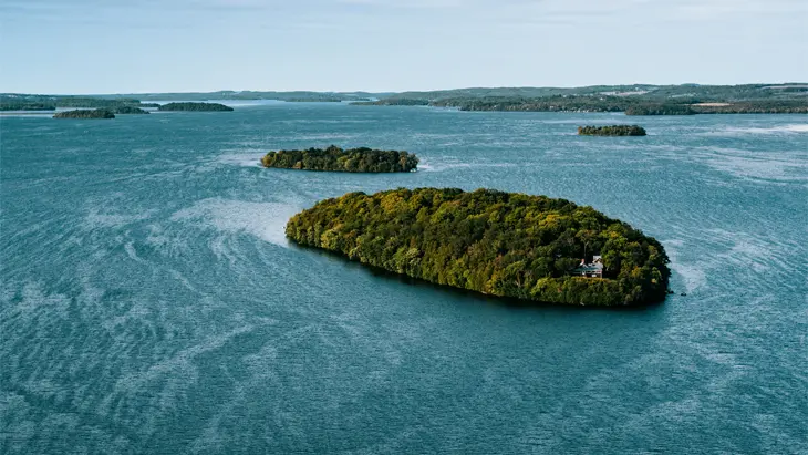 라이스 호수에 있는 코버그의 공중 사진. 푸른 바닷물에 둘러싸인 무성하고 나무로 뒤덮인 섬과 멀리 보이는 작은 섬들을 보여줍니다.