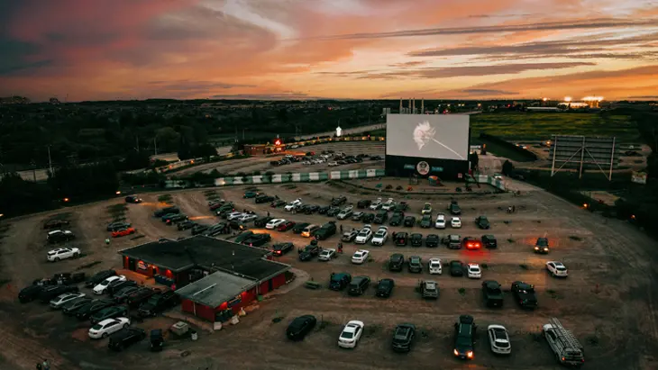 夕暮れ時のオークビルの 5 ドライブイン シアターに駐車した車の航空写真。3 つの大きな屋外スクリーンと木々が駐車場を囲んでいます。