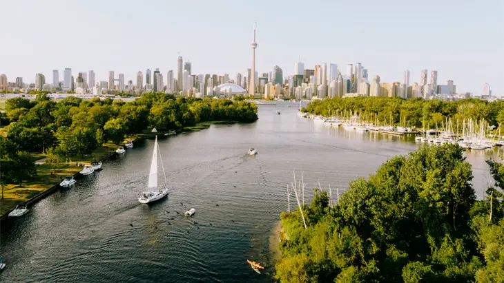 Vue aérienne de la silhouette de Toronto avec la Tour CN, des bateaux sur l’eau et une végétation luxuriante.