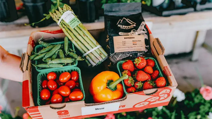 Boîte de produits frais remplie de haricots verts, de tomates, d’asperges, de poivrons orange, de fraises et de marc de café à Meuse Farm &amp; Market.