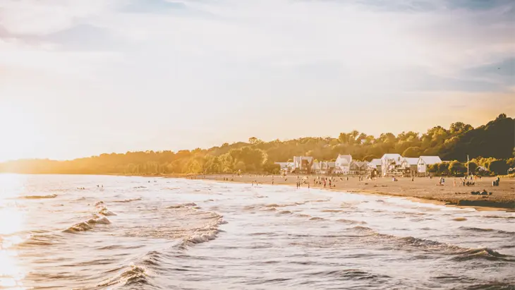 穏やかな波と海岸線を楽しむ人々、柔らかな金色の空の下、ビーチの端に並ぶ趣のある家々が見える夕暮れ時のポート スタンレー ビーチの眺め。