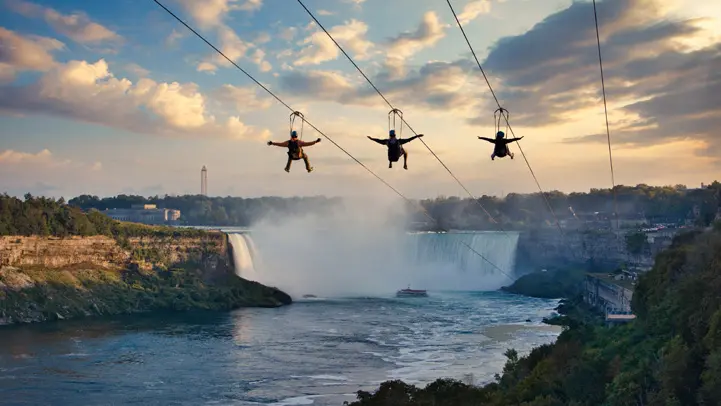 Three people take a thrilling zipline ride towards the Niagara Falls at WildPlay Zipline.