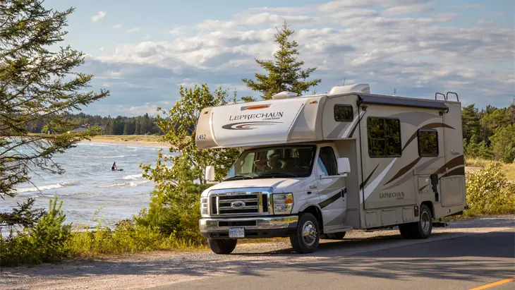 An RV driving on a highway with a body of glistening water beside it, in Little Current, Ontario.